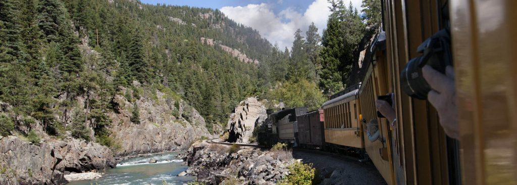 train-next-to-river-and-mountains-1024x366